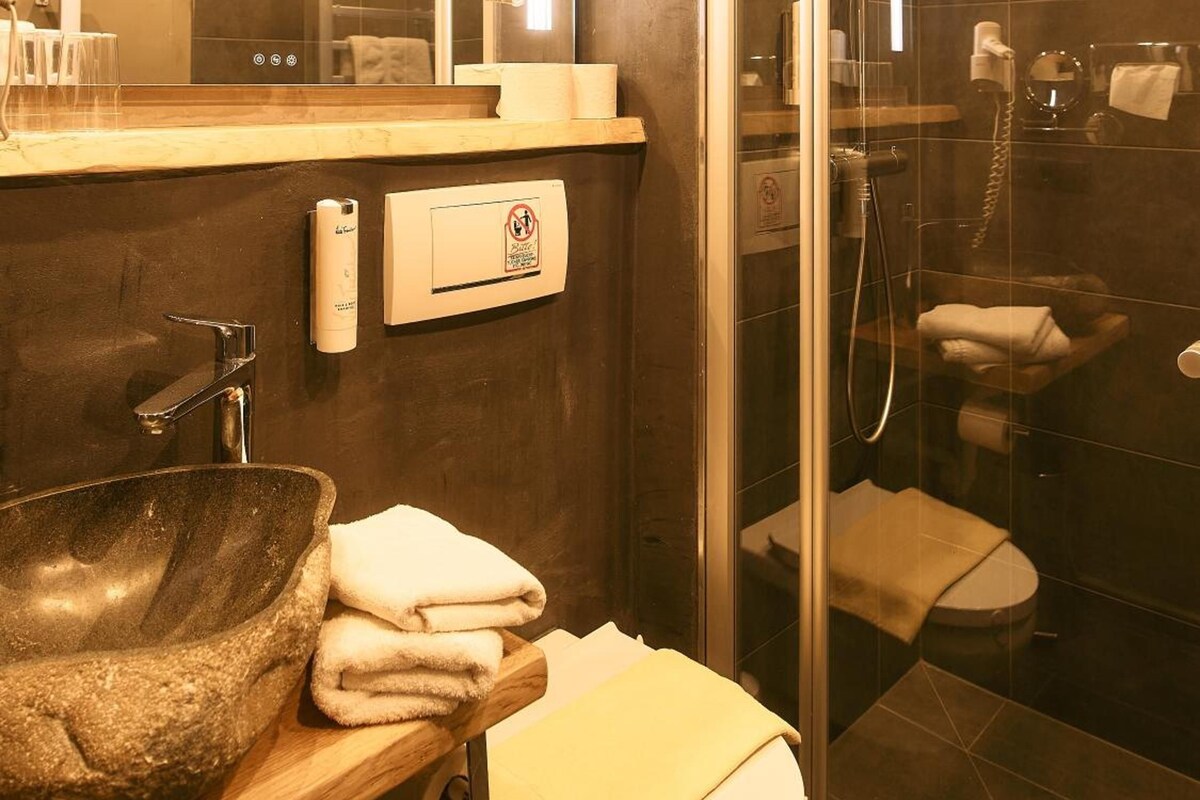 Un baño moderno con ducha envuelta en cristal, lavamanos de piedra y un inodoro.