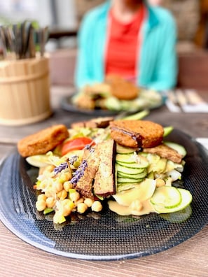 Un plato con ensalada, garbanzos, rodajas de pepino y palitos de pan.