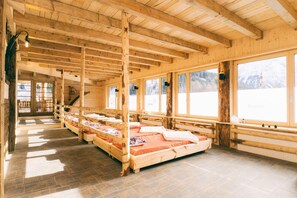 Una cabaña de madera con varias camas dispuestas en filas, ventanas amplias y piso de baldosas de piedra.