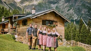 Eine Holzhütte mit Steinunterbau, umgeben von einem Holzzaun, vor einer Bergkulisse gelegen.
