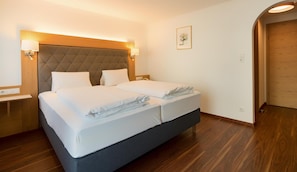 A hotel room with a double bed, bedside lamps, a wooden headboard, a small bedside table, and a framed picture on the wall.