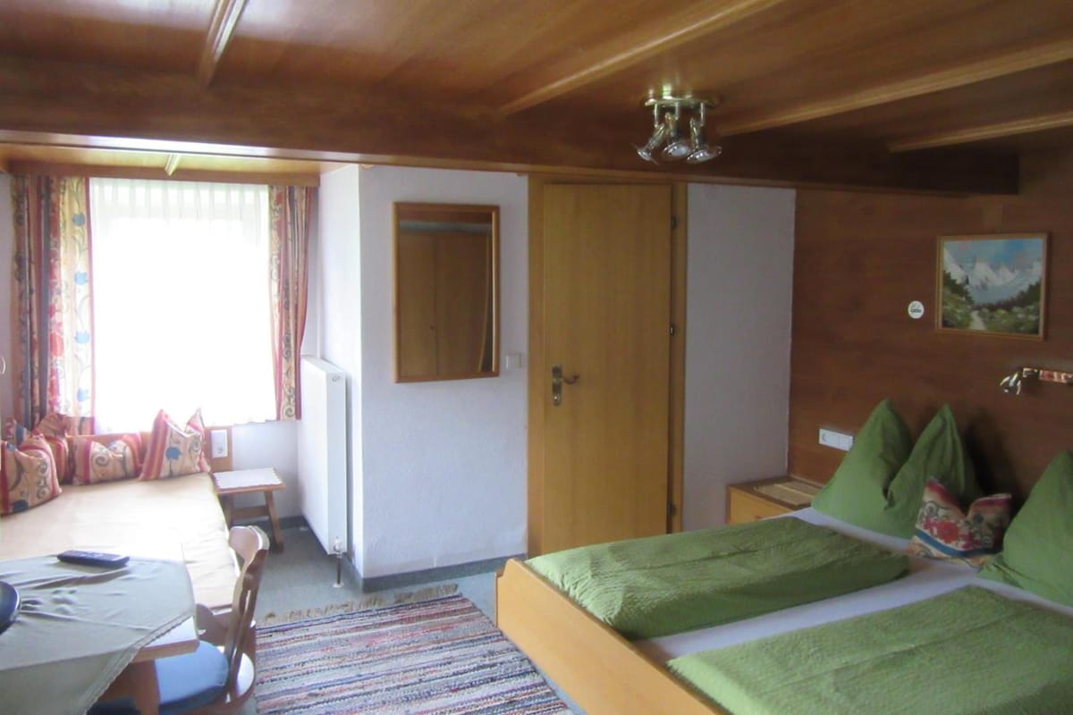 A hotel room with a bed, a desk, a chair, a window with curtains, a mirror, and a painting on the wall.