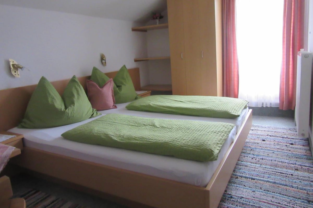 A hotel room with a bed, pillows, a wardrobe, and a window with curtains.