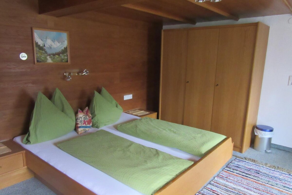 A bedroom with a wooden bed, green pillows, a painting on the wall, and a wardrobe.