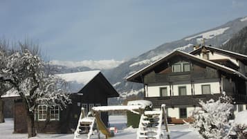 A snow-covered mountain landscape with a wooden chalet and a playground in the foreground.