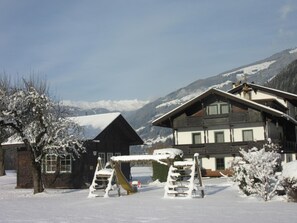 A snow-covered mountain landscape with a wooden chalet and a playground in the foreground.