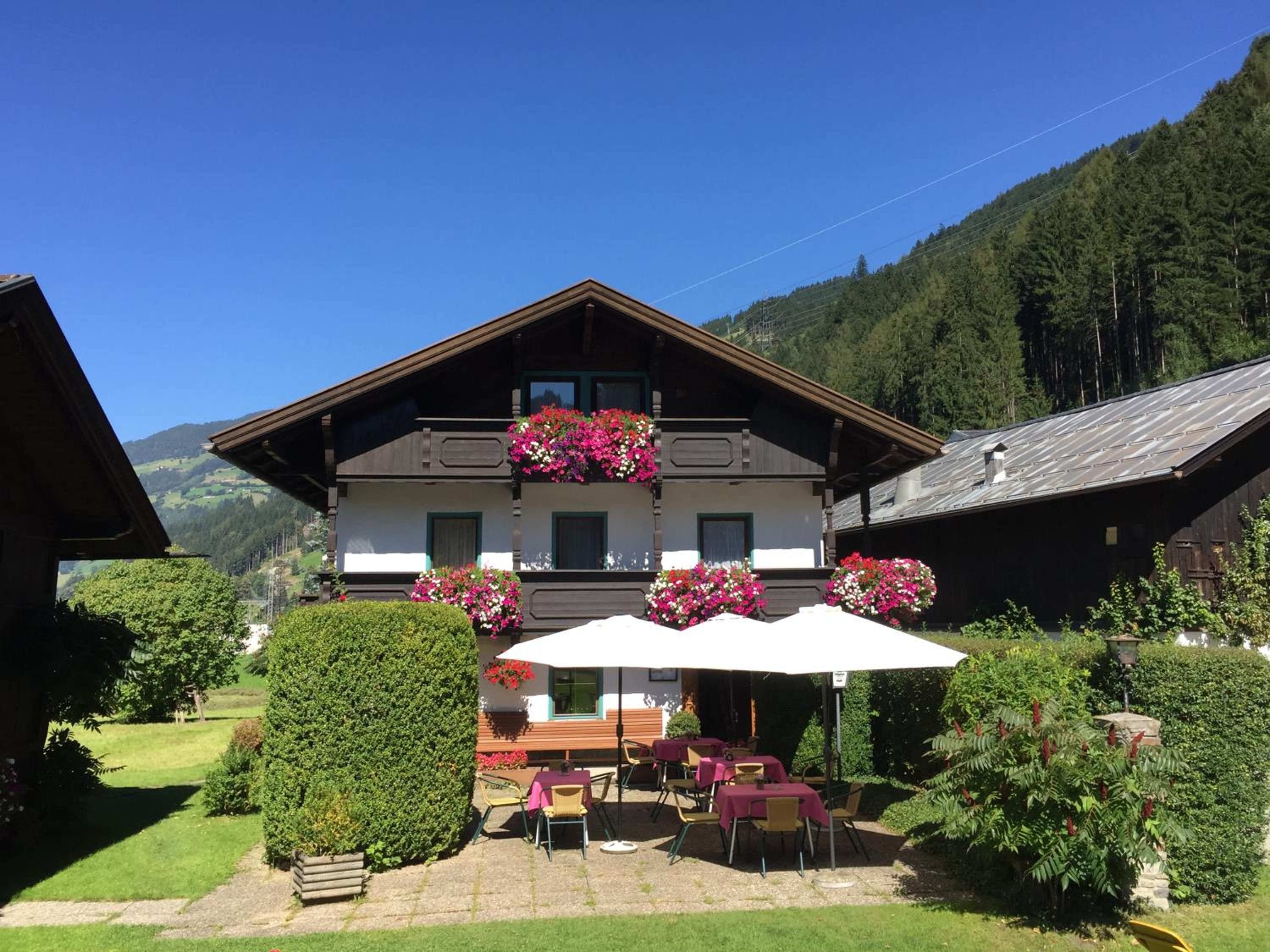 Un chalet tradicional con un balcón decorado con flores, mobiliario de exterior y vistas a un paisaje montañoso.