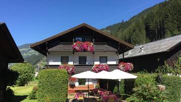 A traditional chalet with a balcony adorned with flowers, outdoor seating, and a view of a mountainous landscape.