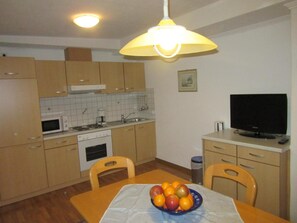 A compact kitchen with wooden cabinets, a microwave, a stove, and a dining table with a fruit bowl.