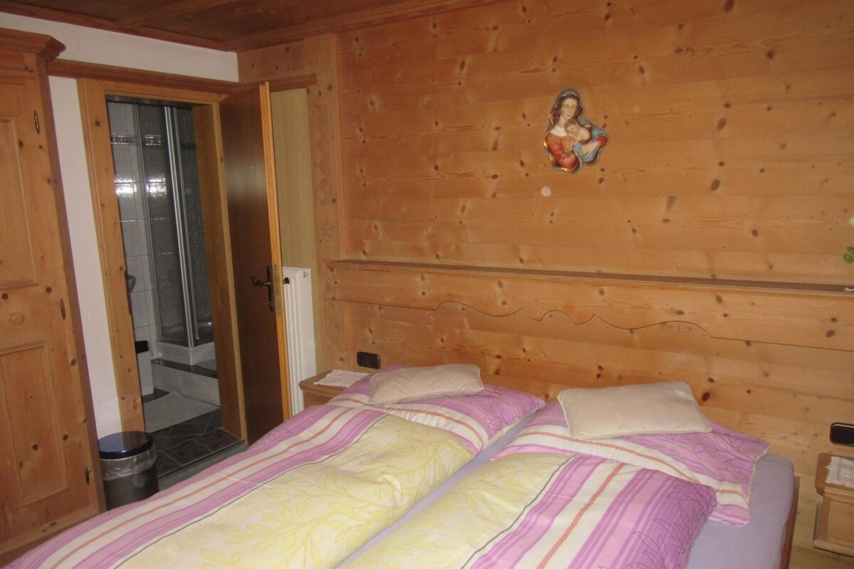 A bedroom with a wooden headboard, a bed with striped bedding, and a small religious figure decoration.