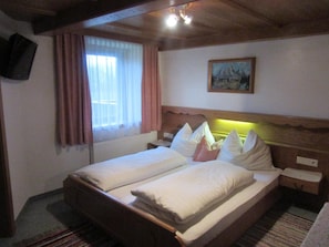 A double bed with a wooden headboard, a painting on the wall, and a window with curtains.