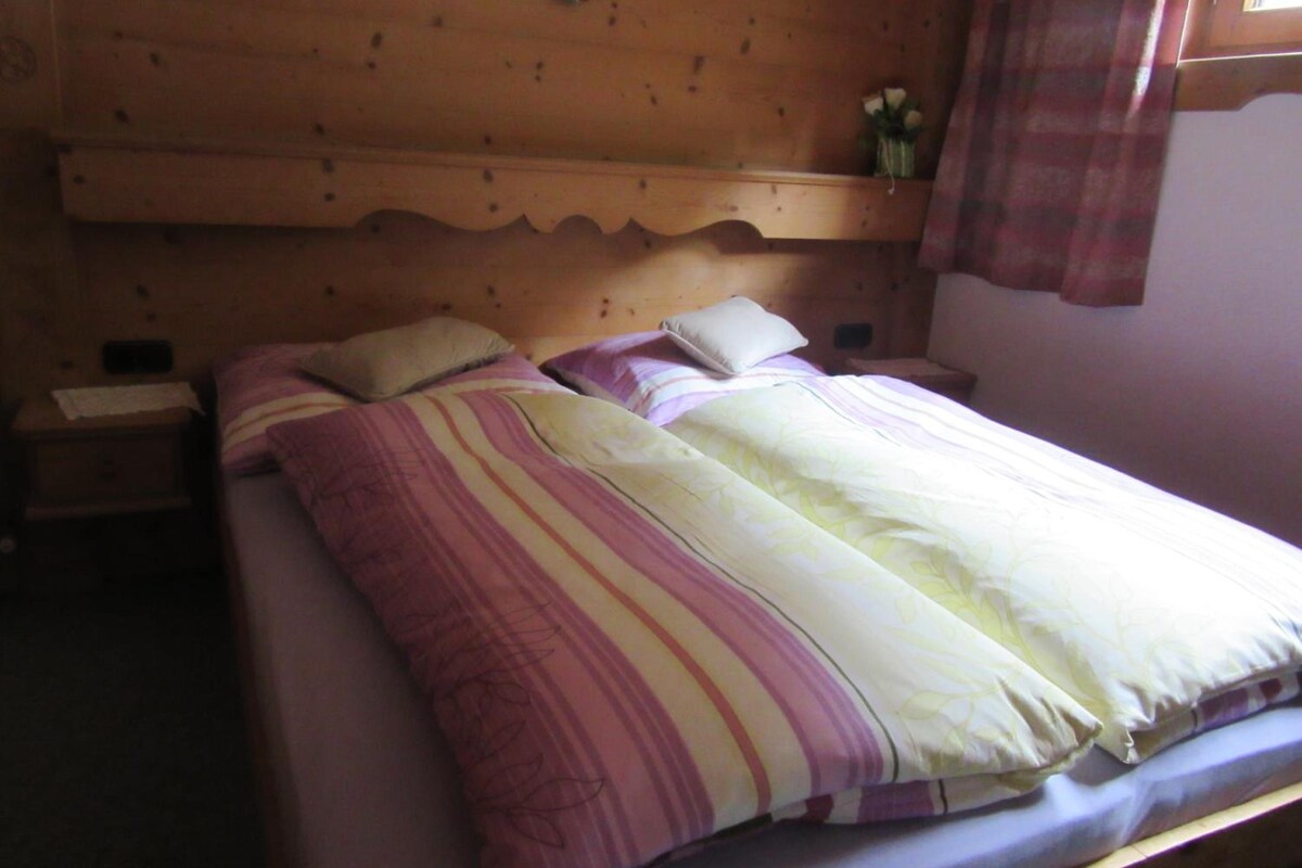 A single bed with a wooden headboard, two bedside tables, and a small shelf with flowers.