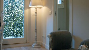 Een kamer met een houten vloer, een lamp, een stoel en een raam met uitzicht op groen.