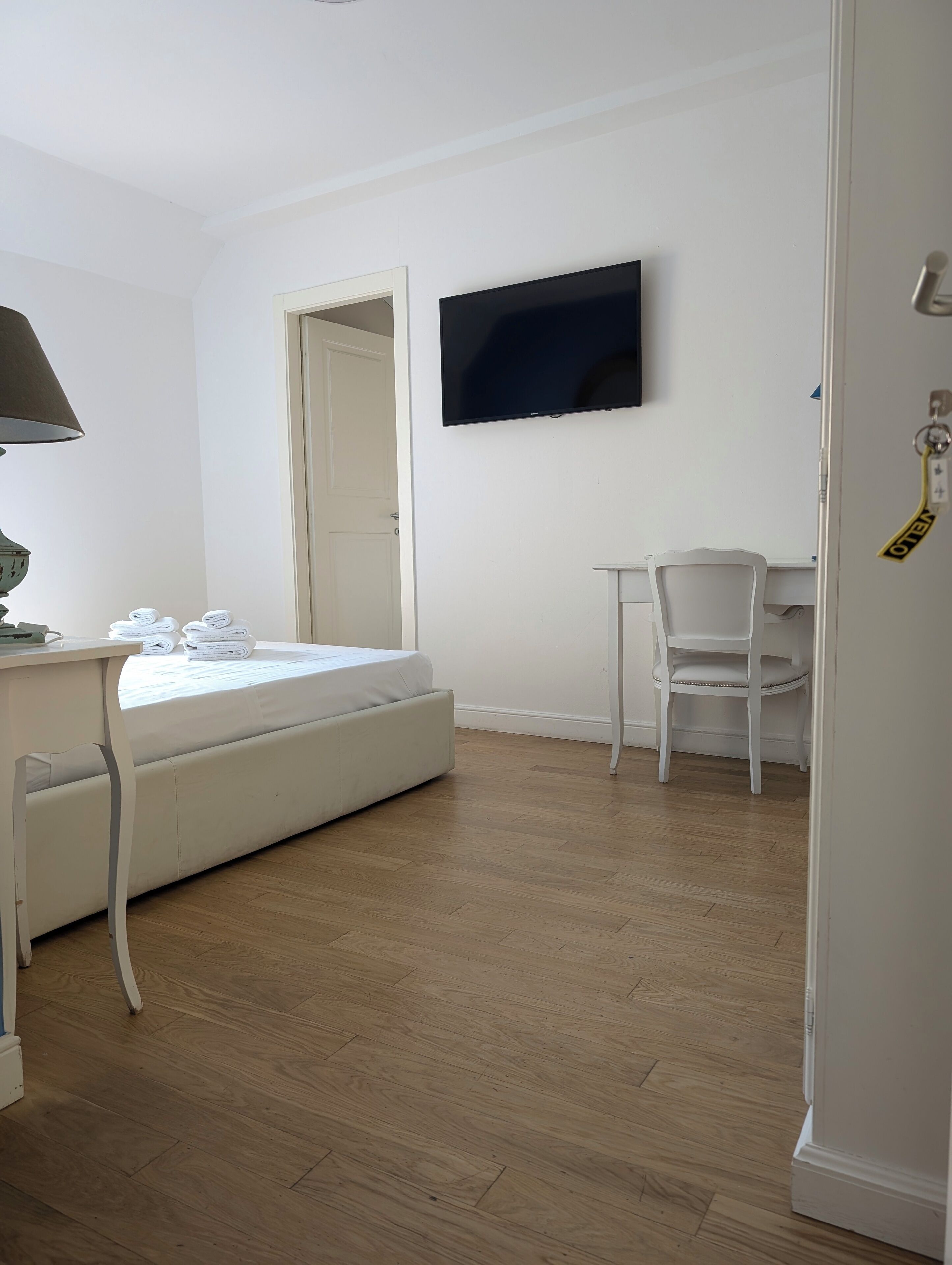 A room with a bed, a desk, a chair, a television, and a door.