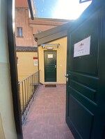 En bygningseingang med en grøn dør, et skilt med værelsesnumre og en lille balkon med gelænder.