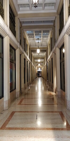 A long, narrow hallway with a polished floor, large windows on both sides, and a central chandelier. - Cosmopolitan Central Rooms (Bologna)