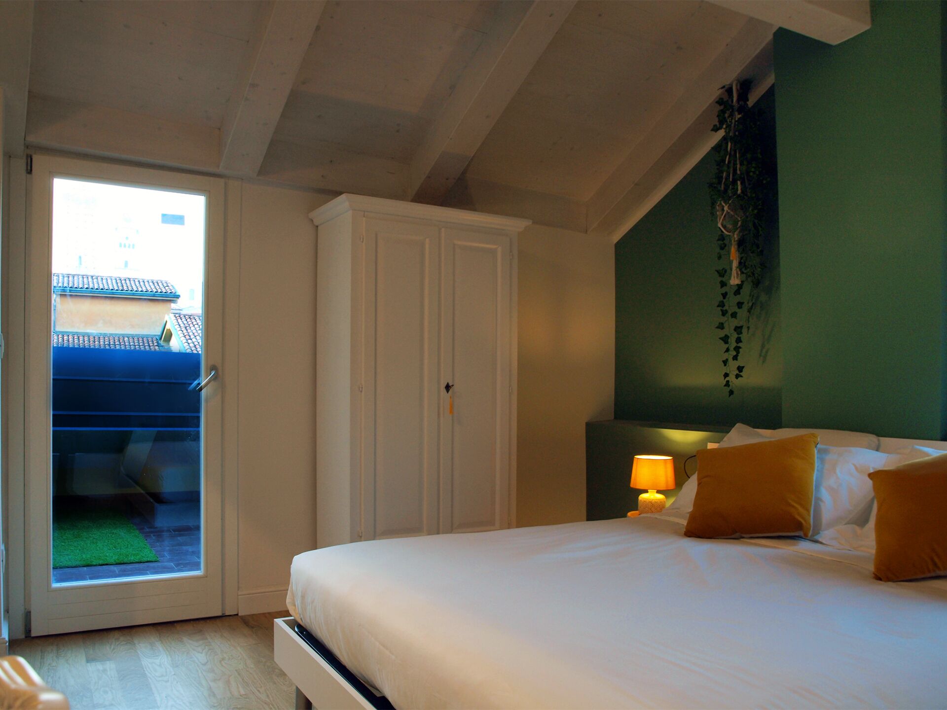 Een slaapkamer met een bed, nachtkastje, lamp, kledingkast en een schuifdeur naar een buitenruimte.