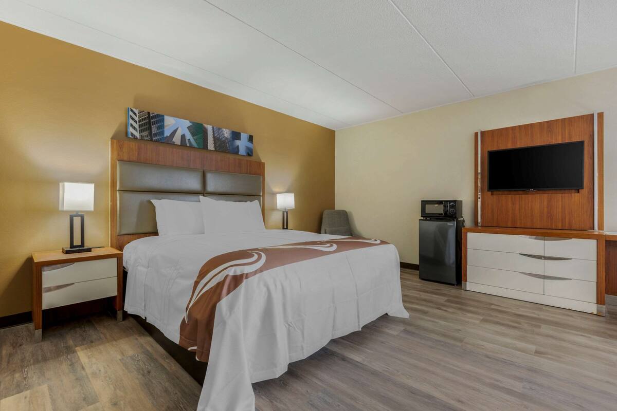 A hotel room with a bed, bedside tables, a desk, a television, and a refrigerator.