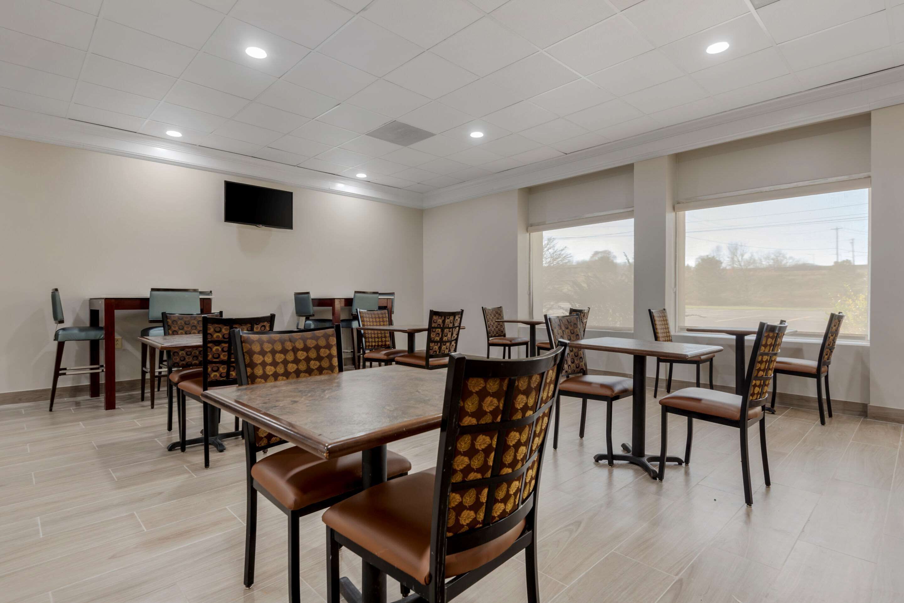 Une salle de conférence dotée de plusieurs tables et de chaises, d’un téléviseur à écran plat fixé au mur et de grandes fenêtres laissant entrer la lumière naturelle.