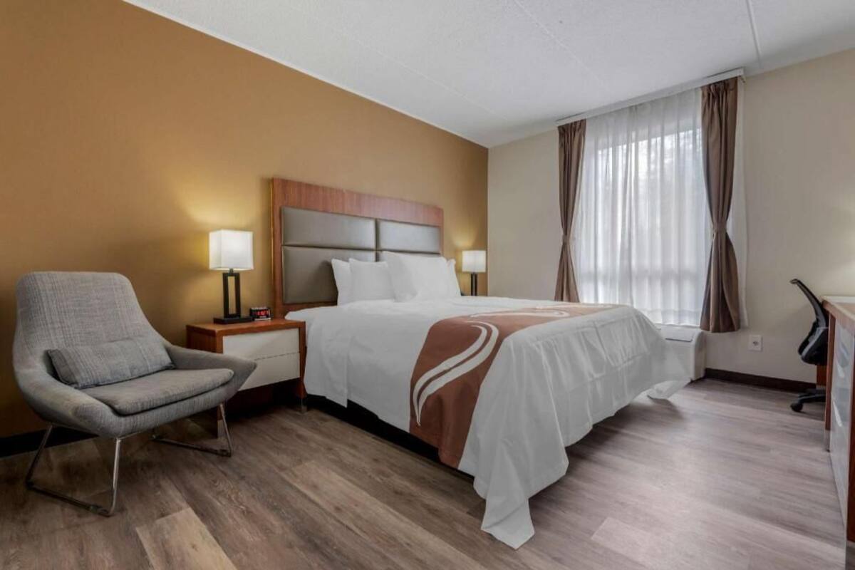 A hotel room with a bed, a chair, a desk, and a lamp.