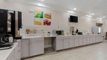A modern kitchen area with a coffee machine, microwave, and various food items on the counter.