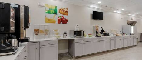 A modern kitchen area with a coffee machine, microwave, and various food items on the counter.