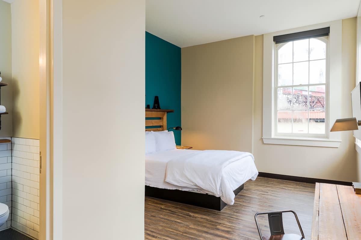 Une chambre à coucher avec un lit, une table de chevet en bois, une fenêtre donnant sur un beau paysage et un plancher en bois.