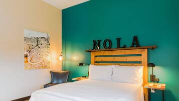Habitación de hotel con una cama, un cabecero con el nombre 'NOLA', un mapa en la pared y dos mesitas de noche con lámparas.