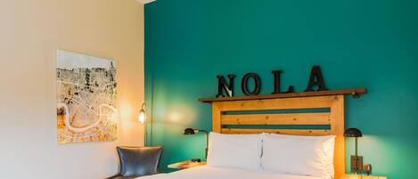A hotel room with a bed, a headboard with the name 'NOLA', a wall map, and two nightstands with lamps.
