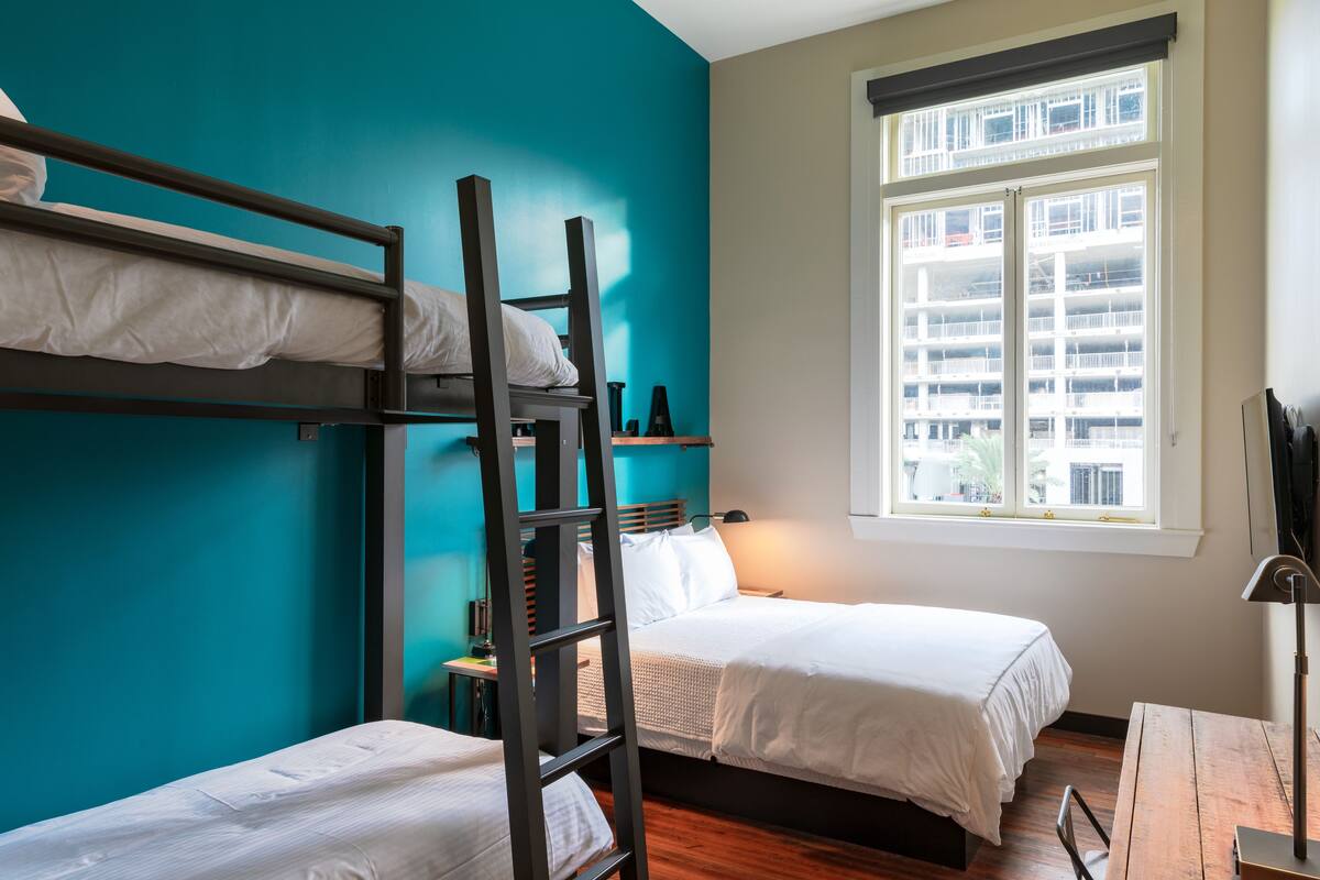 Une chambre de dortoir avec des lits superposés, un bureau et une fenêtre donnant sur des immeubles.