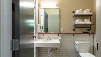 A bathroom with a white sink, a toilet, and a mirror above the sink. There are towels stacked on a shelf above the mirror.