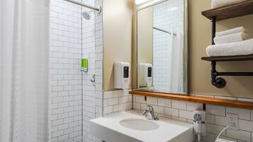 A modern bathroom with a white sink, a mirror, a towel rack, and a shower area.