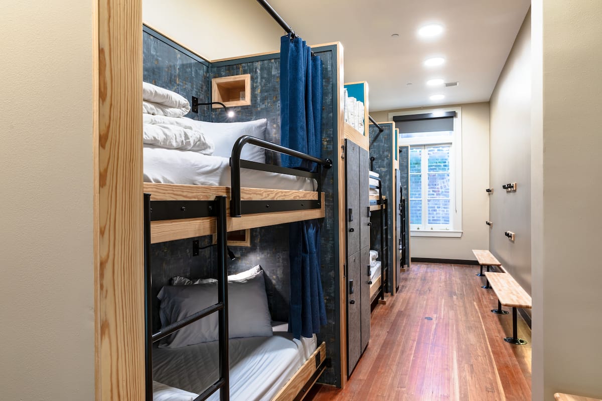 Une chambre avec un lit superposé, un plancher en bois, une fenêtre et un banc.