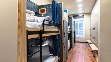 Dormitorio con literas, suelo de madera, una ventana y un banco.
