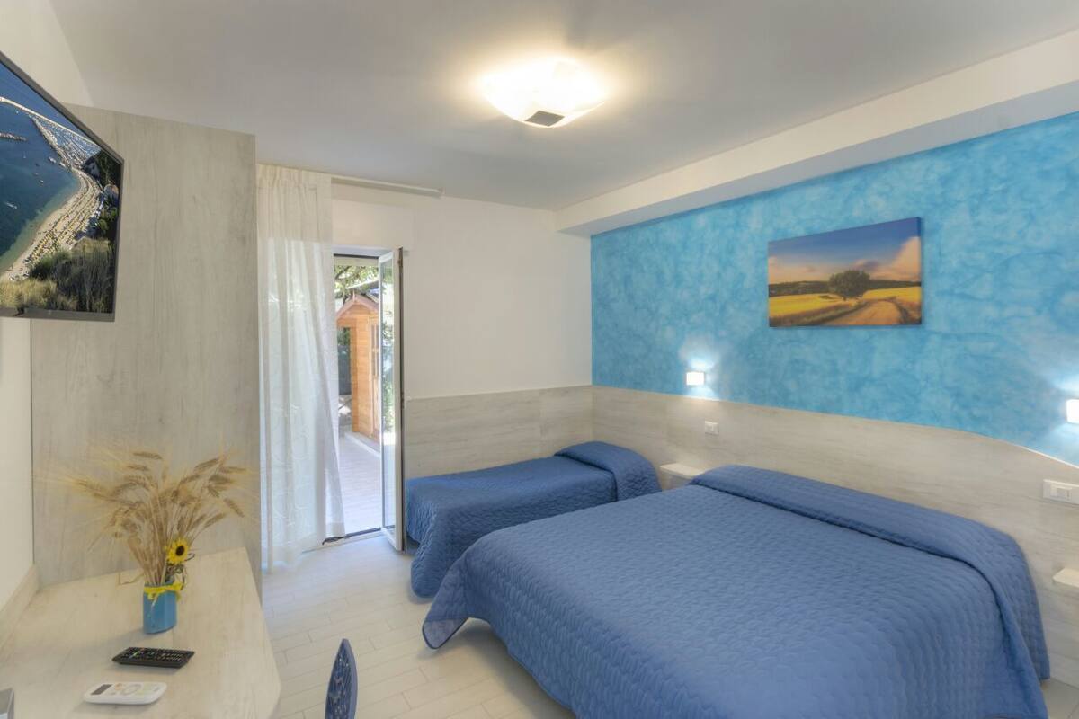 Quarto de hotel com duas camas, televisão, um quadro na parede e vista para a praia pela janela.