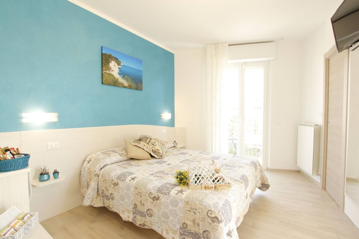 Quarto com cama, parede azul, janela e radiador.
