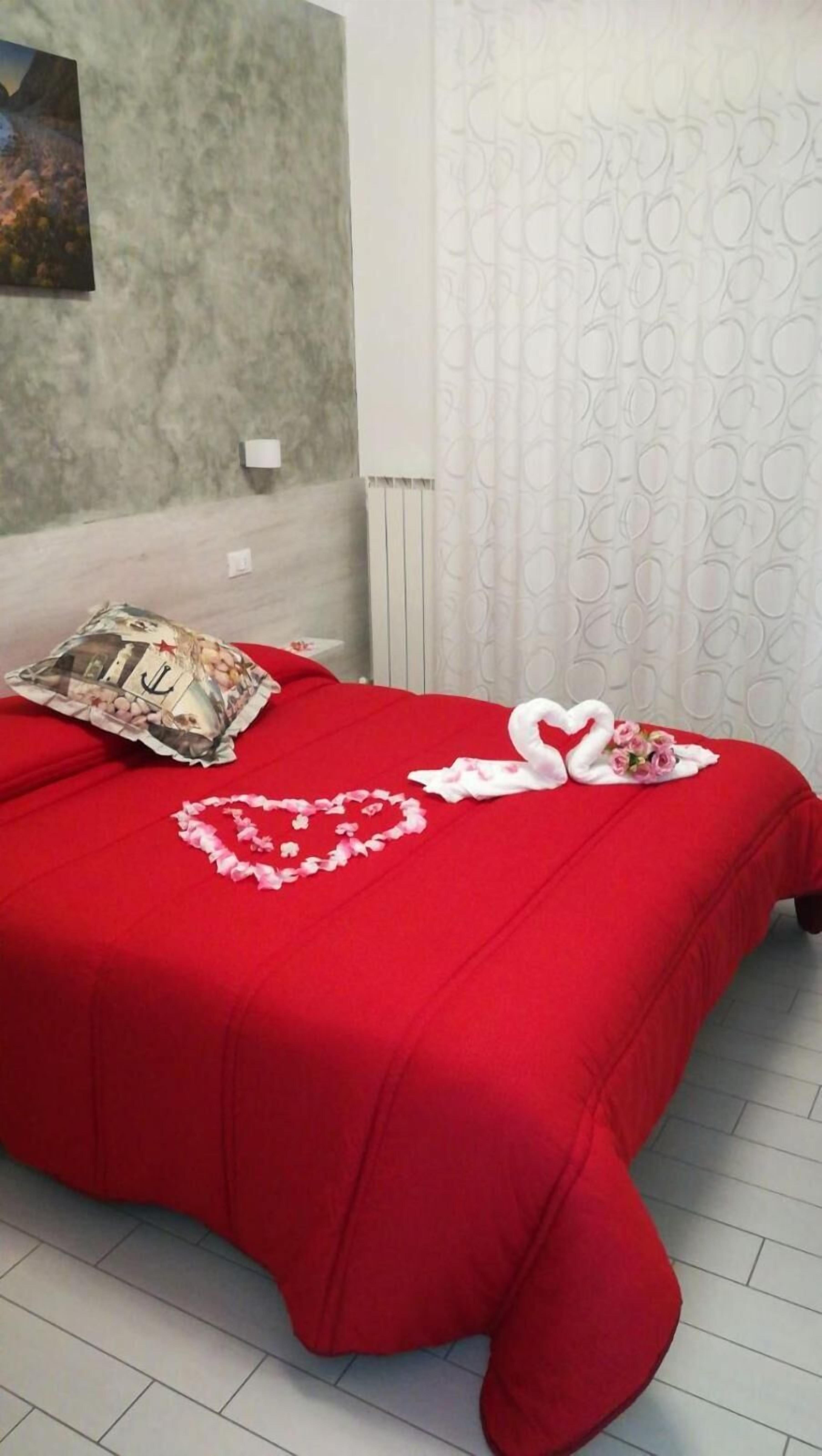 Ein Bett mit roter Bettdecke, ein Kissen mit Anker-Motiv und herzförmige Blumendekorationen.