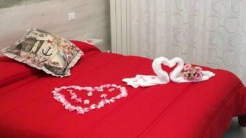 Ein Bett mit roter Bettdecke, ein Kissen mit Anker-Motiv und herzförmige Blumendekorationen.