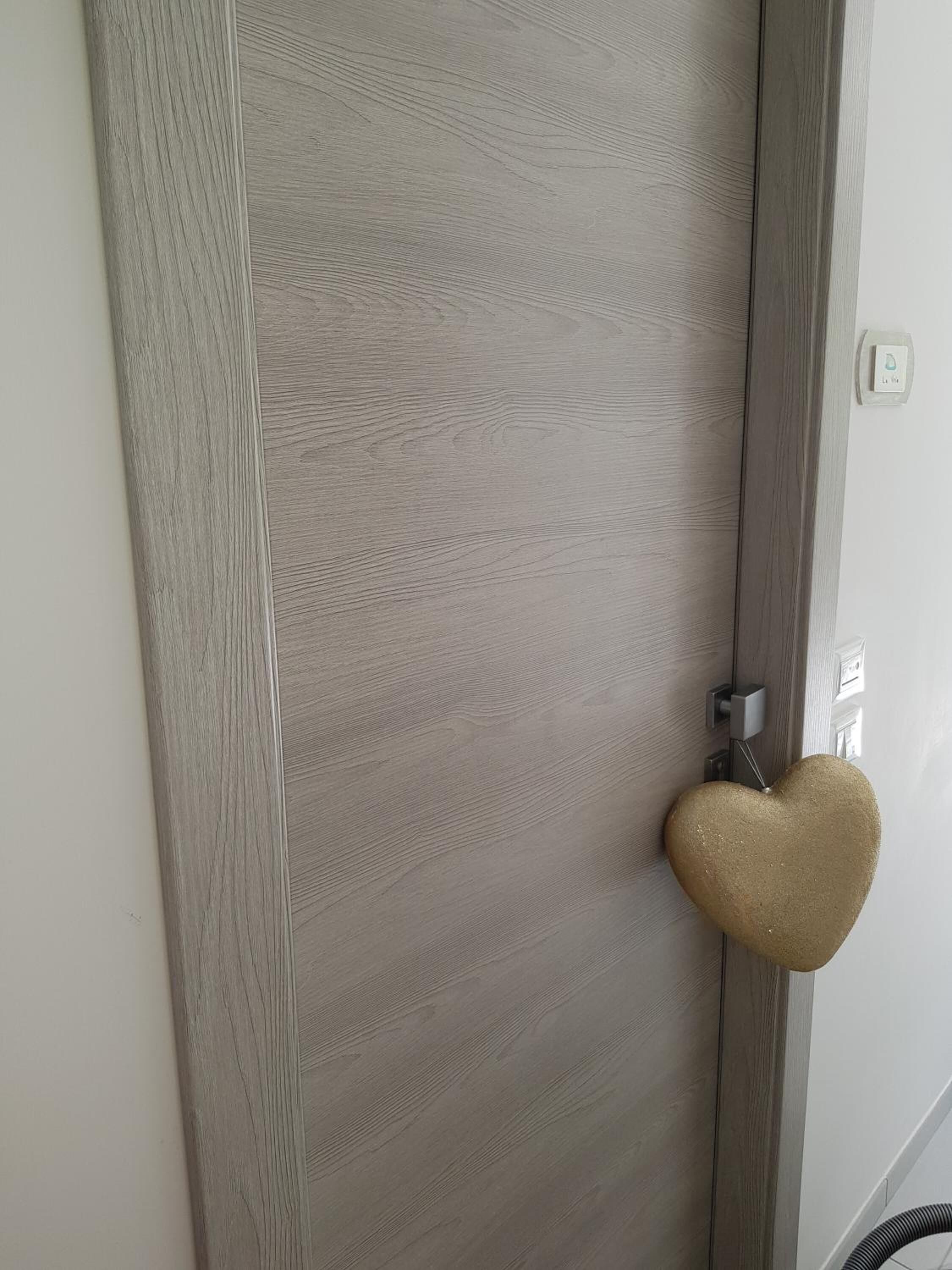 Una puerta con acabado gris texturizado y un llamador con forma de corazón.