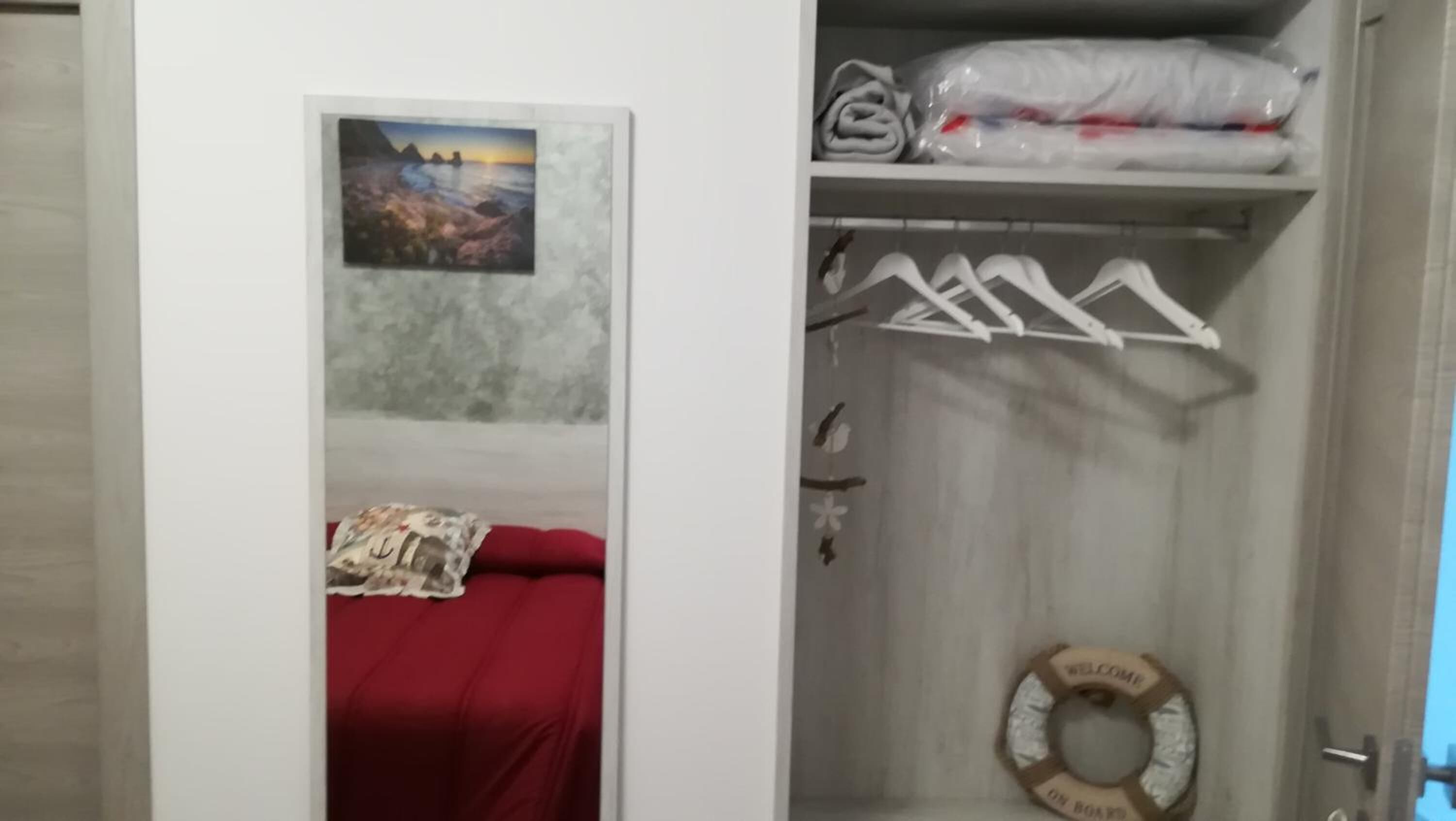 A room with a bed, a closet with hanging clothes, and a life preserver on the floor.