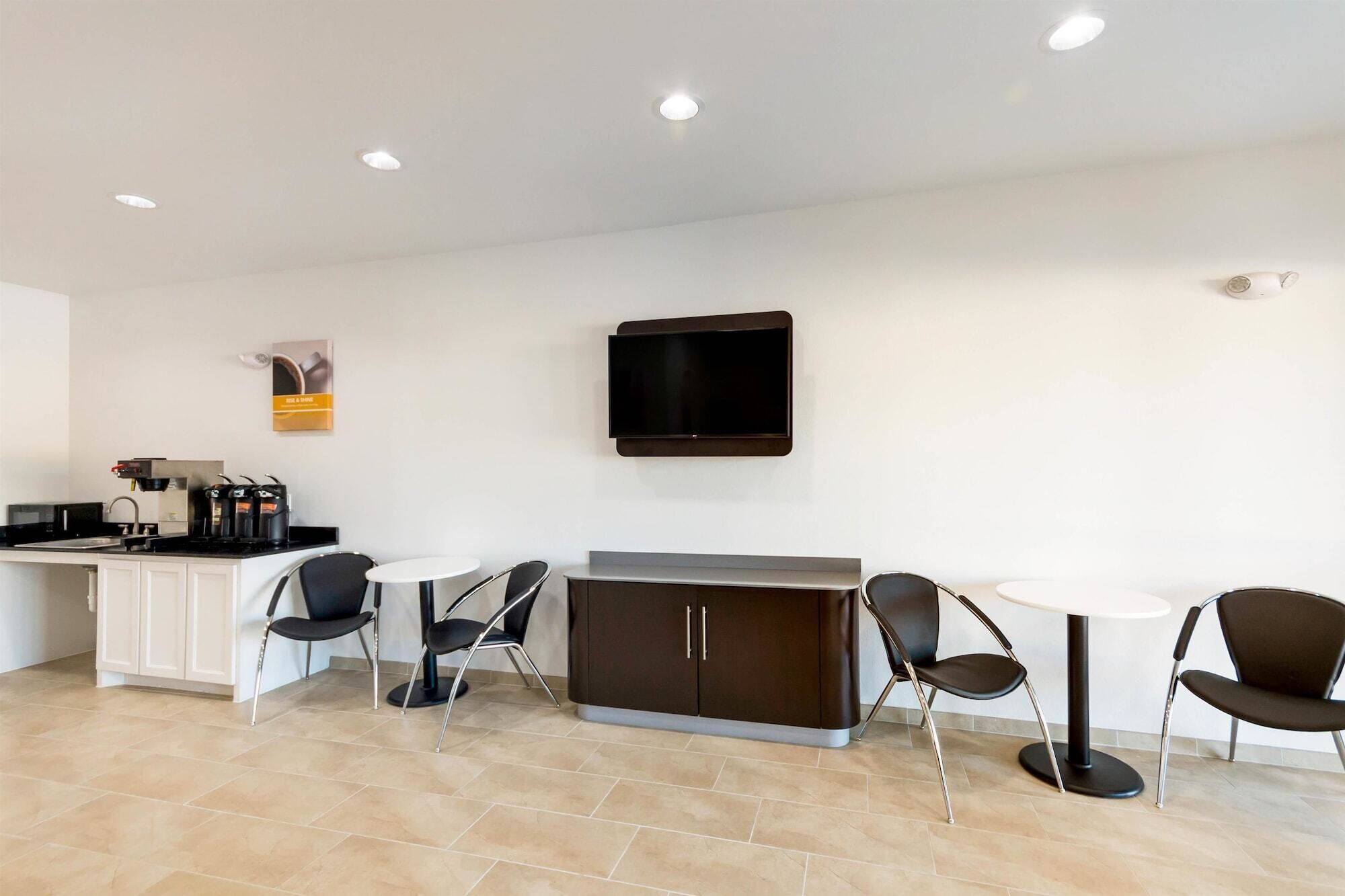 A modern kitchen with a built-in stove, a microwave, and a coffee machine. There are four black chairs around a small white table, and a TV mounted on the wall.