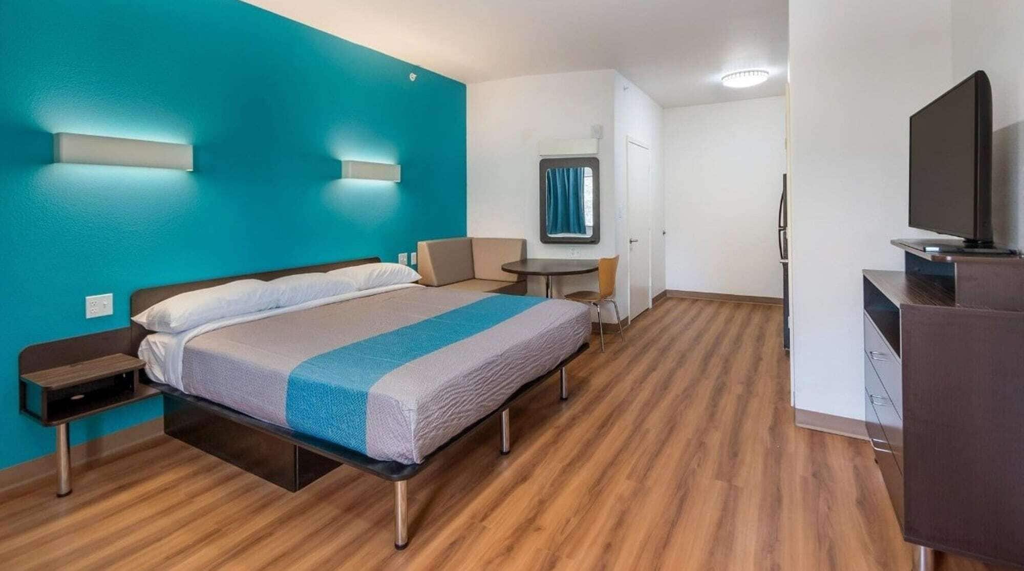 A hotel room with a bed, a desk, a chair, a TV, and a small table.