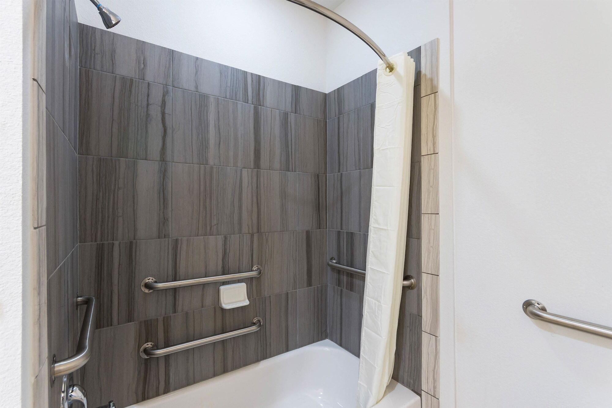 Une salle de bain moderne avec un espace douche, des barres d’appui et une baignoire blanche.