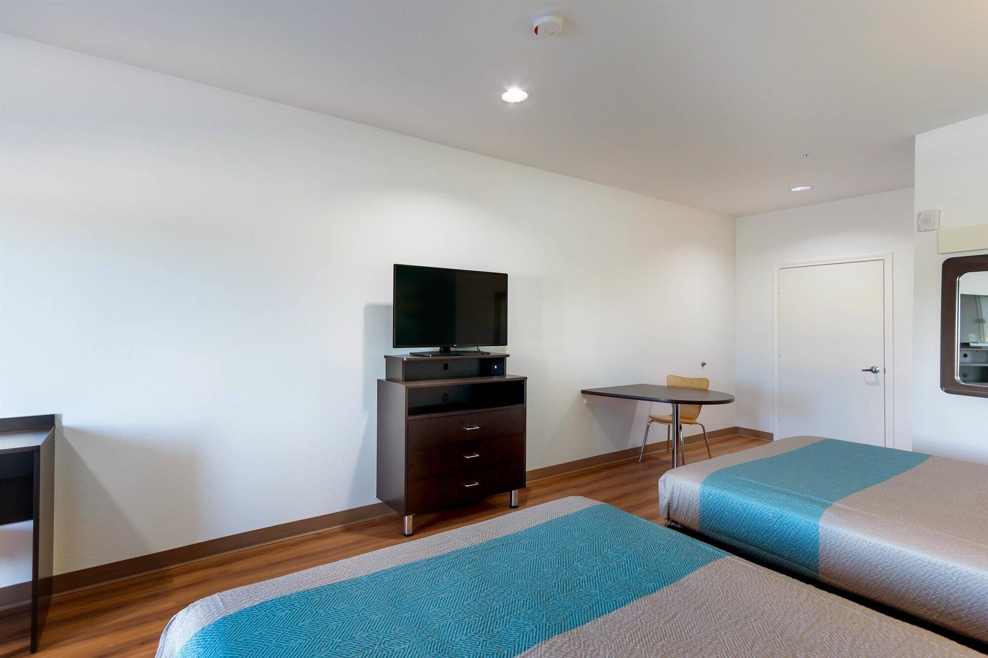 Une chambre d’hôtel avec deux lits simples, un bureau avec une chaise, un téléviseur posé sur un meuble et une petite table.