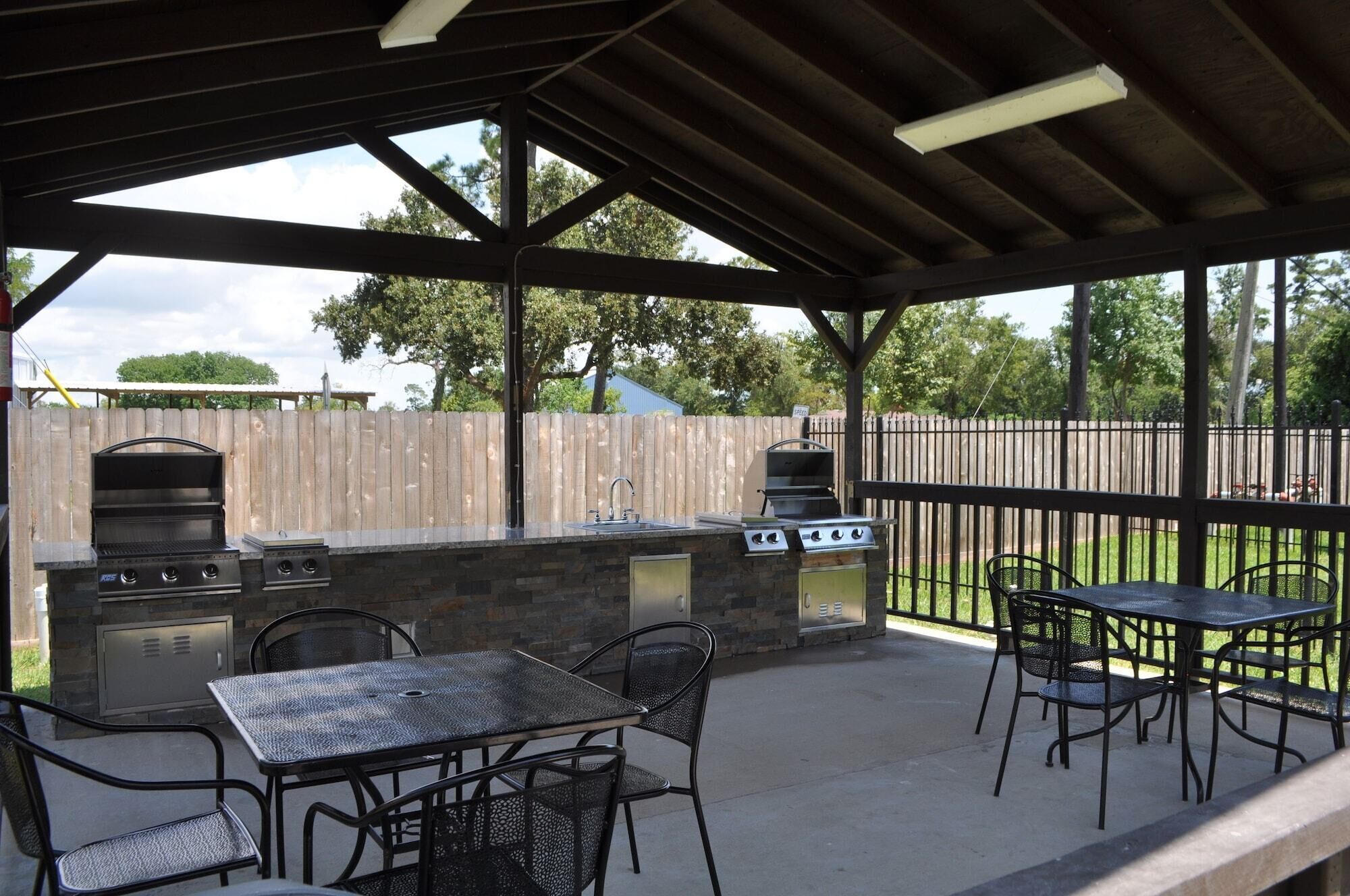 An outdoor patio with a stone barbecue and grill station, a metal table and chairs, and a wooden fence in the background.
