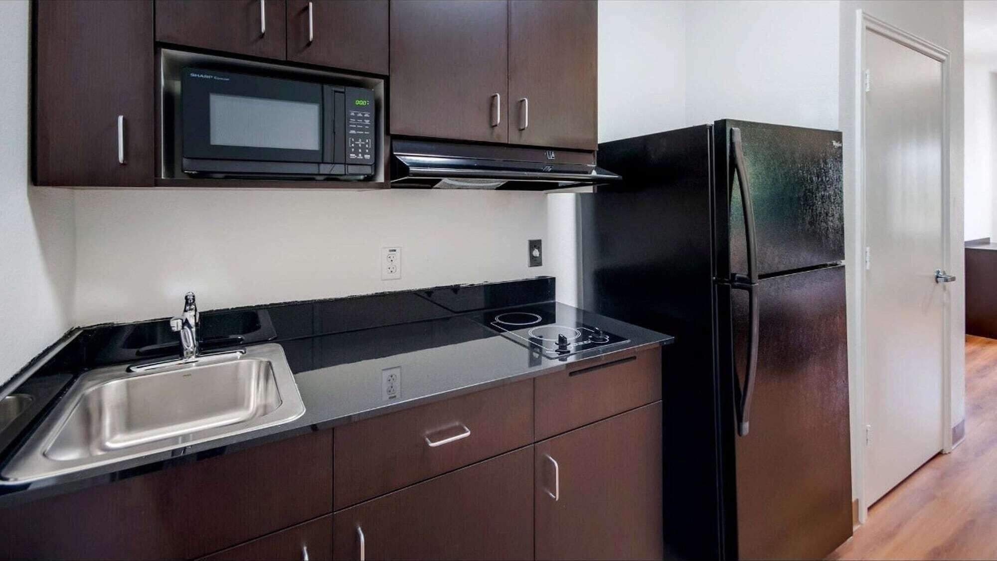 A modern kitchen with dark cabinetry, a stainless steel sink, a black microwave, and a black refrigerator.