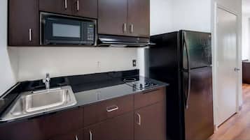 A modern kitchen with dark cabinetry, a stainless steel sink, a black microwave, and a black refrigerator.