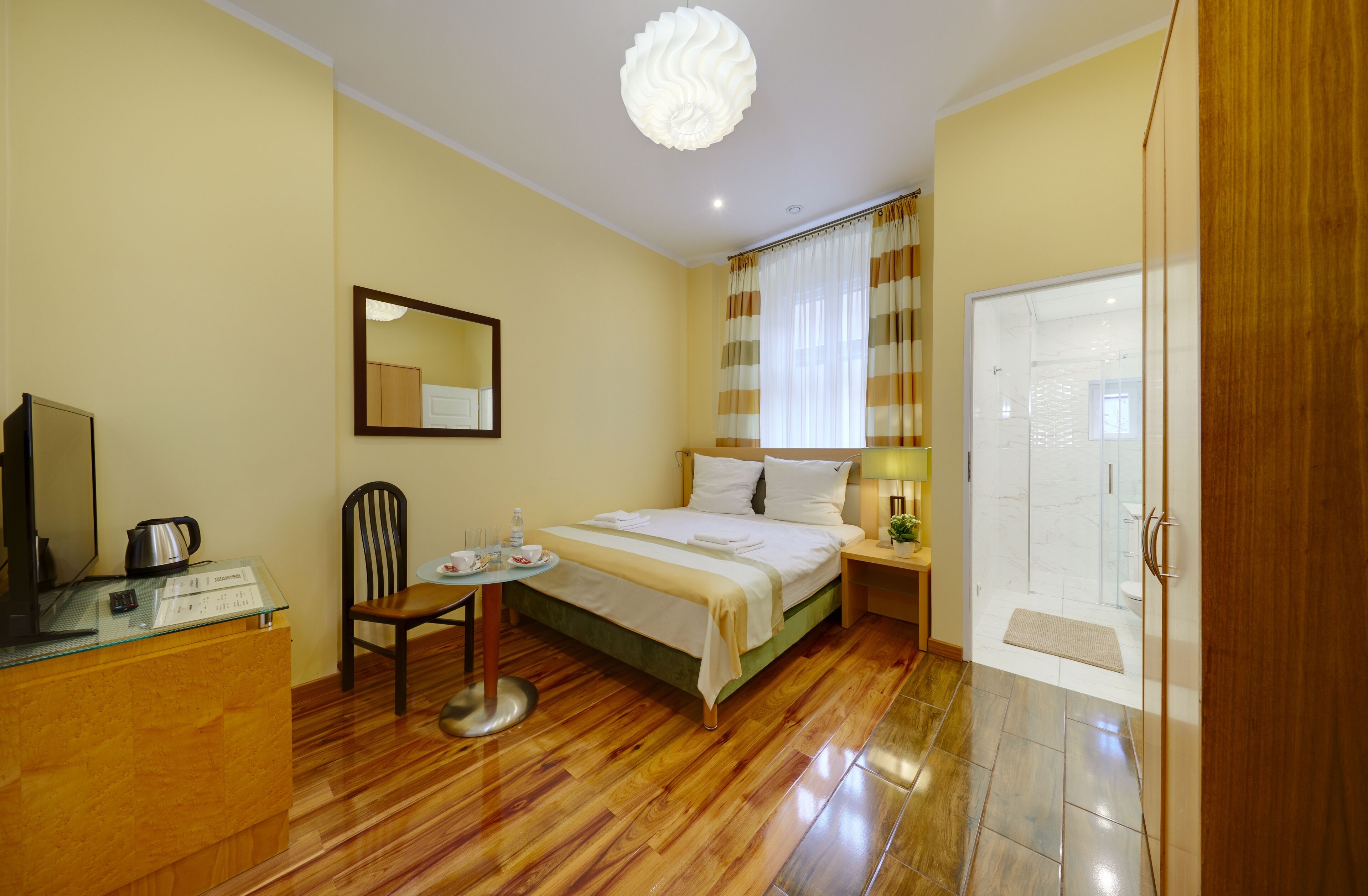 A hotel room with a bed, a desk, a chair, a mirror, a lamp, and a door.