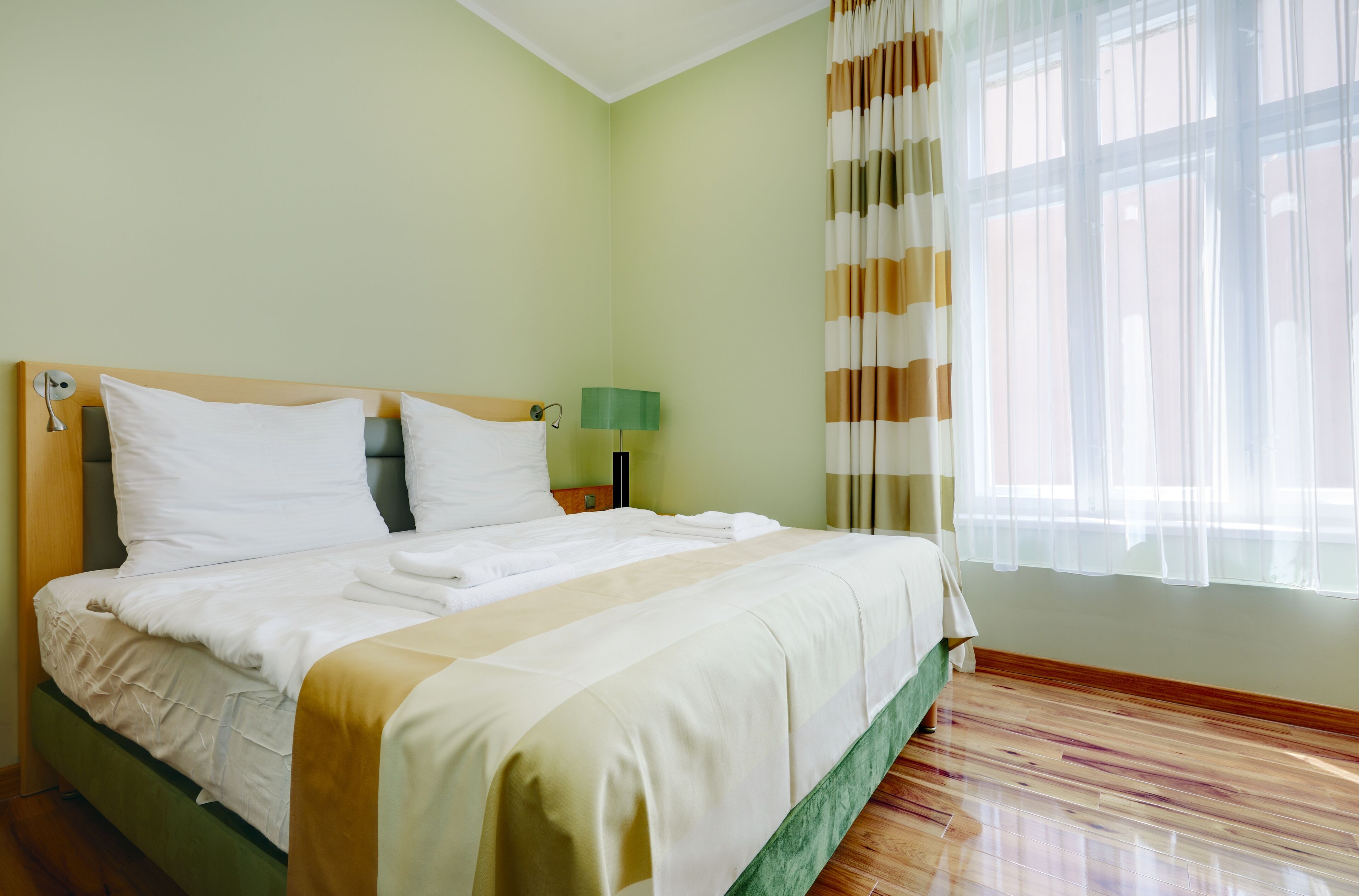 A neatly made bed with white linens in a room with green walls and wooden flooring.