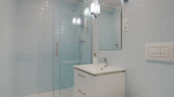 A modern bathroom with a glass shower enclosure, a white sink, and a toilet.